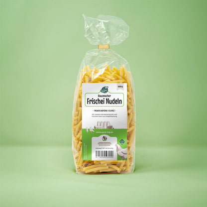 Frontalansicht von Hausmacher Frischei Nudeln Makarroni kurz 500 Gramm in einer Plastiktüte mit Etikett.
